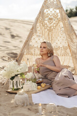 A beautiful blonde girl of Slavic appearance. On the sand is a  macrame wigwam, pillows and...
