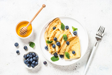 Crepes with blueberries and honey in white plate at white stone table. Top view with copy space.