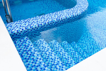 Steps in the pool with blue ceramic tile mosaic. Relax in the backyard of a country house
