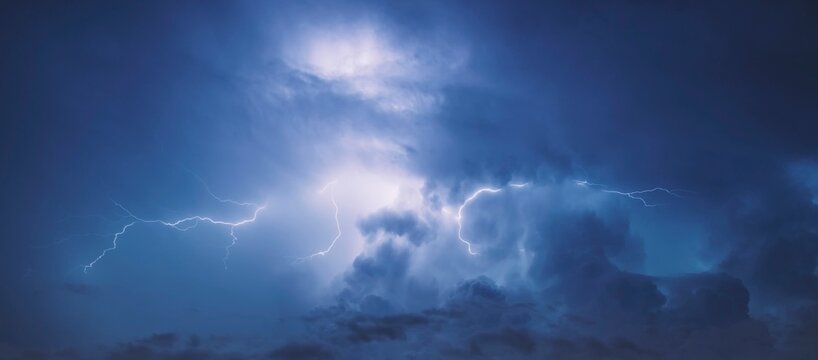 Lightning in the blue sky with clouds at night.