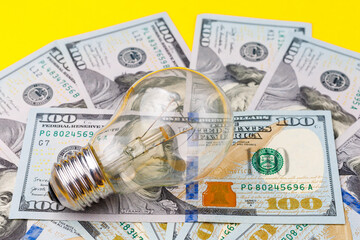 Classic electric light bulb on a blurred background of dollar cash bills or banknotes