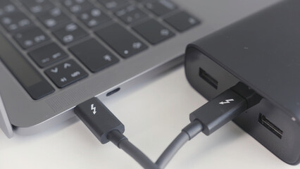 Black portable external power bank, for emergency device recharge. Action. Close up of an open laptop is charged with a power bank via a cable, portable modern devices, external battery, cable, USB