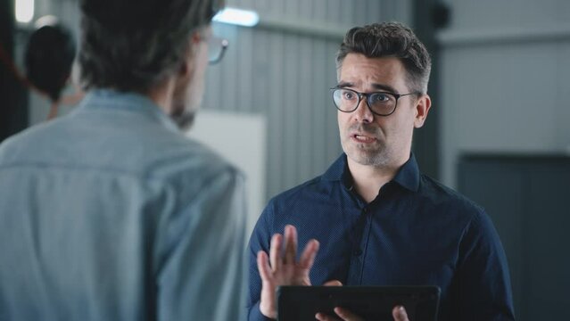 A manager in a suit and glasses with a tablet standing with a client in a car service, and communicating about car diagnostics and checking