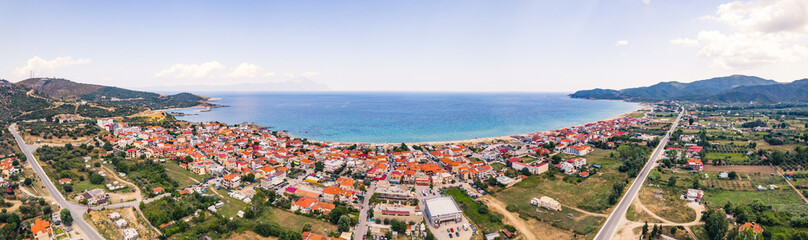Long panoramic aerial drone shot of Greek seashore presenting green area in the small city of Sarti. Whitewashed houses with red roofs. High quality photo