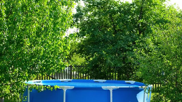 Metal frame pool in backyard of a private house. Blue swimming pool on green lawn with trees background.