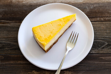 Slice of Lemon Cheesecake on white plate on wooden background