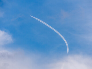 An arcuate trail from a jet aircraft high in the sky. Airplane and cirrus clouds. Vacation or travel concept