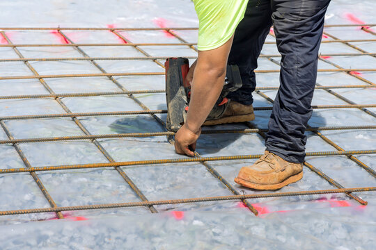 For cement foundation, construction worker twists steel bars with wire rod reinforcement using rebar tying tool that is used to create rebar connections.
