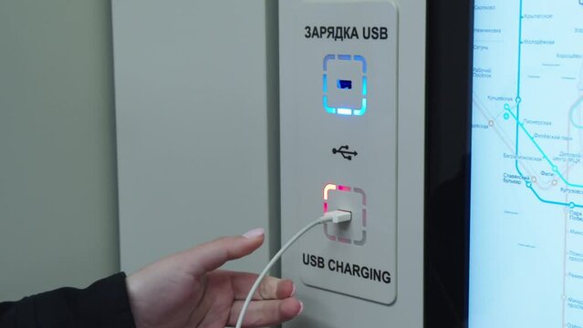 Female hand is plugging the usb cable to the free charging port with russian and english title in modern subway car. usb charging in moscow metro train.