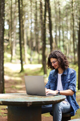 Young latin man sitting in the forest working with laptop freelancing looking laptop at Costa Rica