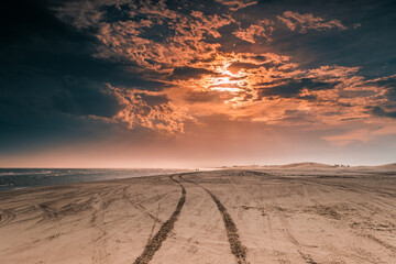Obraz premium Sunset on the beach, with car tire tracks.
