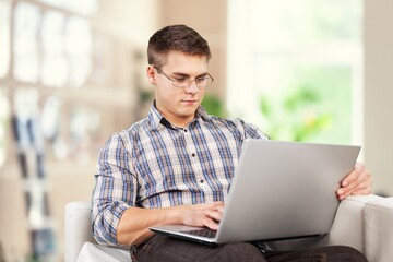 Portrait of smiling man using laptop. Adult male sitting on comfy couch in living room, watching video, taking break