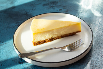 Lemon cheesecake and fork on plate on blue background.