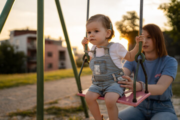 mother and daughter little toddler girl child on swing in park