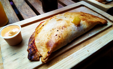 Tasty calzone served on a wooden board with its dressing 





