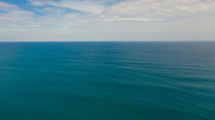 Obraz premium Open blue ocean with waves against the sky and clouds, top view.