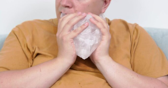 Mature plump man holds cold ice pack in hands trying to cool down on hot summer day. Man contentedly exhales putting ice pack on face closeup