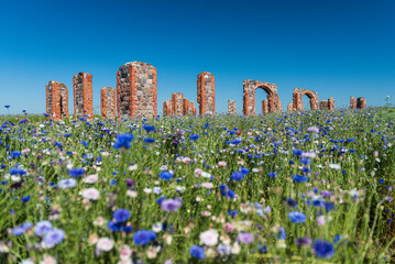 Ruins of an old building that looks like Stonehenge and multicolored (blue, purple, pink, white and other) cornflower flowers (Centaurea cyanus) field in sunny summer day, Smiltene, Latvia. - obrazy, fototapety, plakaty