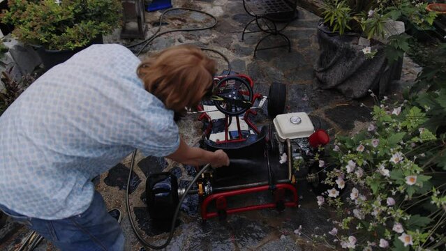 Top down shot of mechanic washing go-kart in his backyard 