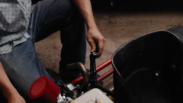 Cinematic shot of mechanic re linking the chain of his DIY go kart with tongs