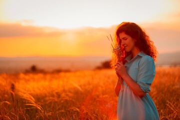 Naklejka premium Woman in the field with flowers on sunset background