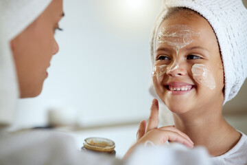 Cute, happy and little girl doing beauty treatment together with her mother. Daughter getting a facial and smiling in the bathroom at home. Adorable child copying her mom, bonding and smiling inside