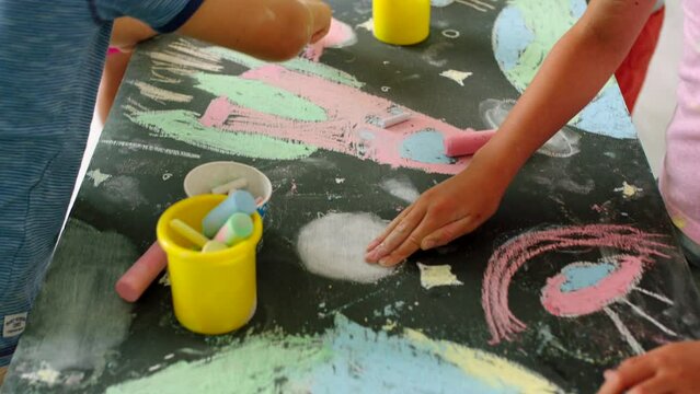Children drawing colourful and creative picture of space, on a board at school. Kids playing, learning and having fun with colouring and art. Imagination development with sketching using chalk.