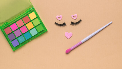 Eyelashes and multi-colored eye shadow with a brush on a beige background. Flat lay.