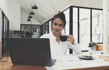 Smiling Asian businesswoman holding a coffee mug and laptop at the office.