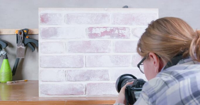 Blonde woman shoots commercial of finishing materials of interiors and exteriors with camera, view from the back. Imitation of brickwork element covered with worn white paint, creating aging effect