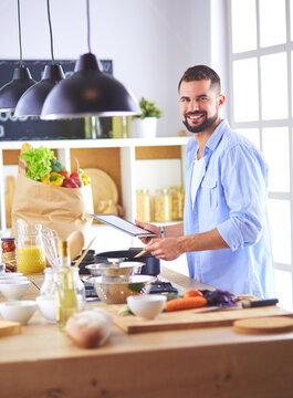 Man following recipe on digital tablet and cooking tasty and healthy food in kitchen at home
