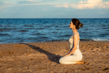 Fototapeta na wymiar Woman practicing yoga outside in hero pose on beach, meditating in sunset
