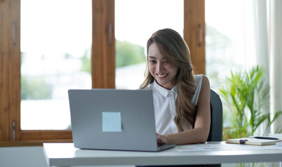 Happy young asian businesswoman sitting on her workplace in the office. Young woman working at laptop in the office.