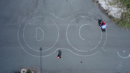 A motorcycle rider practices a figure eight on test track from top down drone view. Instructor can be seen in frame. Sunny to cloudy lighting.