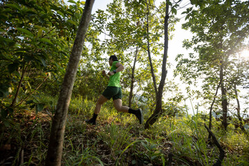 Naklejka na ściany i meble Woman trail runner running at sunrise tropical forest mountain peak