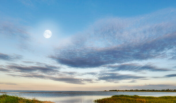 Nature landscape of a cloudy blue sky over the ocean waters. Winter sunrise views on empty calm beach at low tide. Beautiful seaside scene of the natural, peaceful and stressless outdoors.