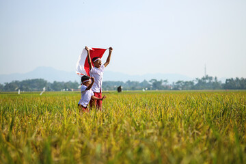 Indonesian school students wearing uniform are raising their hands while holding red white flag in...