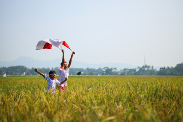Indonesian school students wearing uniform are raising their hands while holding red white flag in...
