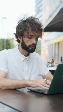 Businessman with makeup using a laptop computer while sitting at a table outdoors.