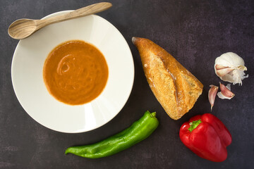 Andalusian gazpacho served in a white plate on a dark background. Tomato, pepper and fresh vegetable soup.