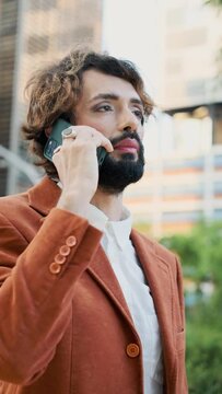 Stylish businessman with make-up smiling while talking on the phone standing outdoors on the street.