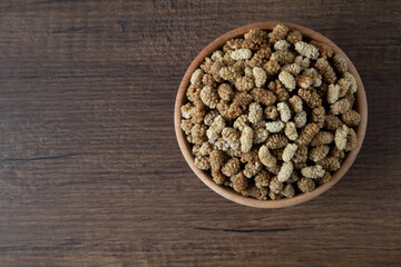 Bowl full of dried mulberry on a wooden background