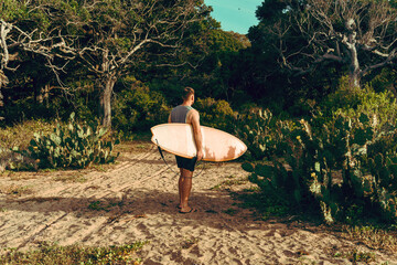 Mężczyzna surfer z deską surfingową, idący wybrzeżem na tle jungle, aktywny wypoczynek. - obrazy, fototapety, plakaty