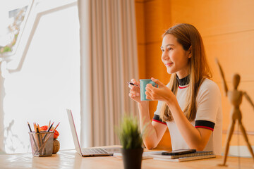 Beautiful ambitious Asian female employee working from home. girl using laptop smile like a dream Students feel inspired to write an essay.