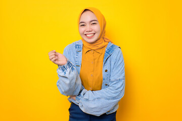 Happy young Asian woman in jeans jacket smiling pleased and looking confident isolated over yellow background