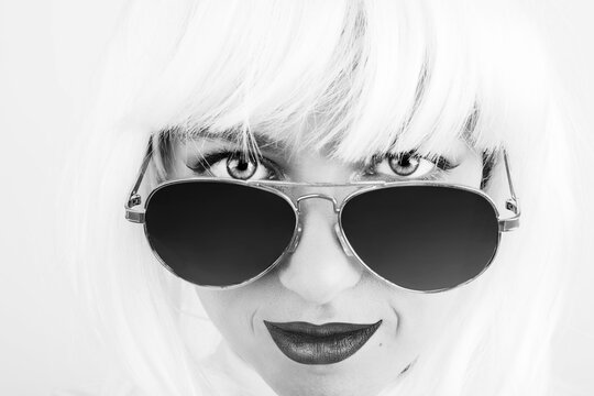 Beauty, fashion and make-up concept. Close-up beautiful woman studio portrait. Model wearing white bob style wig, retro sunglasses and looking into camera with mesmerizing eyes. Black and white image