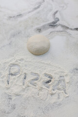 the inscription pizza on the flour near the pizza dough. the word pizza written on the table with flour