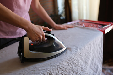 Female housewife ironing crumpled bedsheet on board using steam iron