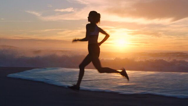 Active, fit female runner running alone at the beach during a beautiful sunset. A healthy young fitness athlete workout with waves in the background. A sports woman exercising in nature by the sea.