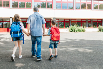 A young dad leads his children by the hand with backpacks on their backs to school. Back to school. Beginning of the academic year and lessons